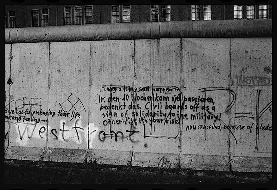 Photographie noir et blanc d'une partie du mur de Berlin avec différents graffitis