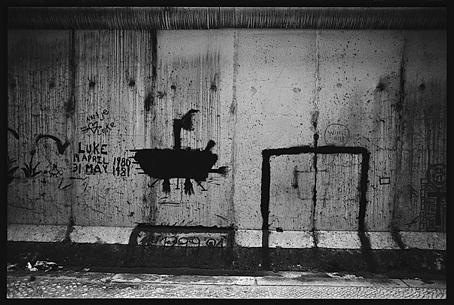 Photographie noir et blanc du mur de Berlin avec différents tag dont un sous-marin noir