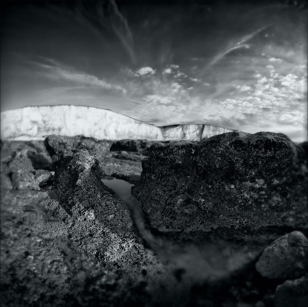 Photographie numérique fisheye en noir et blanc avec un gros rocher en premier plan et la falaise en arrière plan